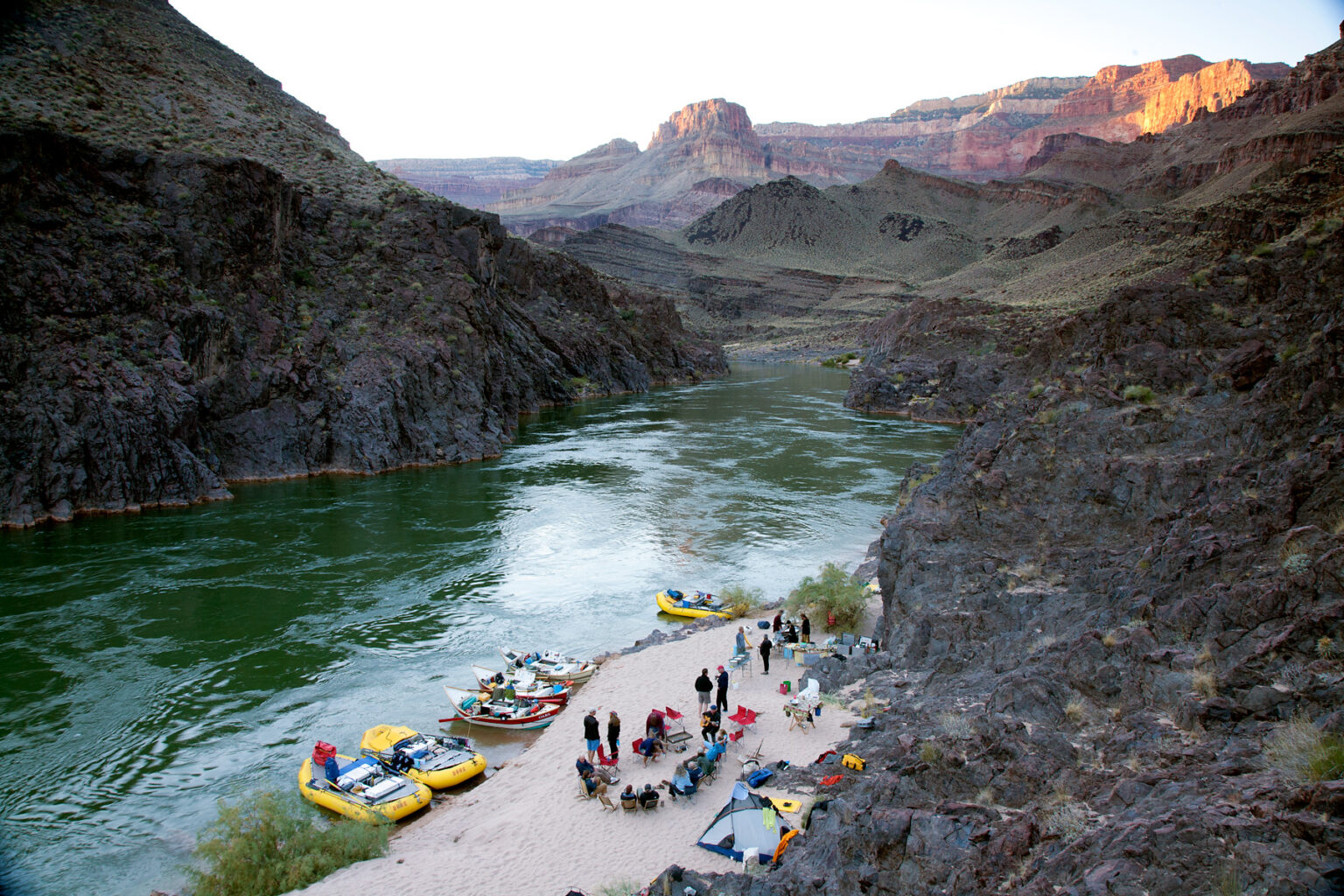 OARS camp from above in Grand Canyon showing moored boats, chair circle, kitchen and tents at sunset