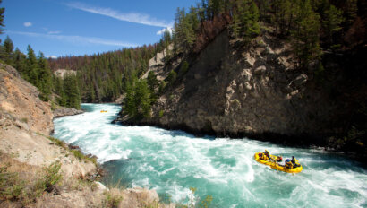 A yellow raft navigates a stretch of rapids on a turquoise blue river frothing with whitewater.